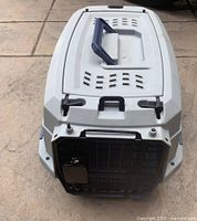Top view of small plastic pet crate showing dark handle on top, ventilation slits, and latch and lock area on front section.