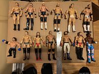 All 13 wrestling figures laid on cardboard in two rows, showing their attire and condition.