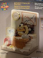 Front view of the boxed 3-D figurine with quartz clock showing Tasmanian Devil and Speedy Gonzales with sales and cost graph behind and a round clock mounted on the wall.