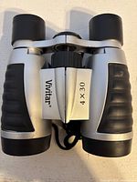 Front view of Vivitar 4 x 30 binoculars showing silver body, black rubber grips, and focus wheel