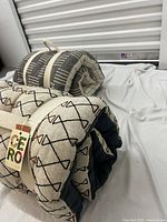 Two rolled tufted mats secured with fabric straps. One has a black geometric pattern on beige fabric and the other has beige lines on black fabric.