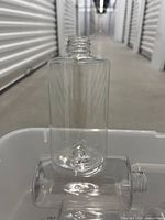 Single clear plastic bottle standing upright on a container with another bottle lying horizontally in front of it.