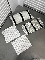 Four throw pillows arranged on the floor showing varying patterns of stripes and geometric shapes in black and white.