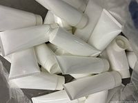 33 white plastic squeeze tubes piled together, showing smooth white surface and screw caps.