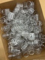Box filled with numerous clear plastic jars, showing quantity and condition.