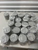 21 grey metal jars sealed in plastic wrap, arranged on a table