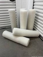 Six white cylindrical bolster pillow inserts standing and laying on a floor.