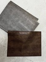 Two folded placemats, one bronze, one pewter, showing textured snake pattern