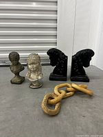 Four decorative items: two bust figurines, winged bookends, and a wooden chain