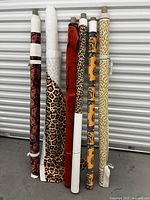 Wide view showing all six rolls of fabric leaning vertically against a white wall, displaying their various patterns and colors.