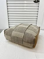 Side and top view showing woven textured fabric with horizontal stripes in beige and cream on the top and leather-like tan material on the bottom.