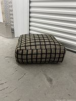 Side view of the square floor cushion showing its height and checkered fabric.