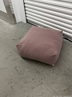 Pink square floor cushion with pin-tucked stitch detailing sitting on concrete floor, shows soft wool fabric and cushion thickness.
