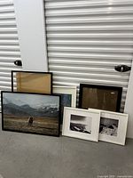 Photo showing several frames of various sizes, some with images and some empty, arranged on a concrete floor against a wall.