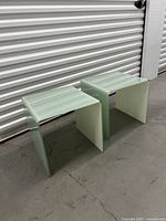 Two U-shaped glass side tables in front of corrugated metal door