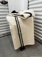 Front view of the cream blanket folded and draped, showing hand stitched black trim and tassels.