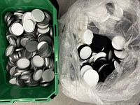 Two bins containing bulk quantities of jar lids in silver metal and black/white plastic.