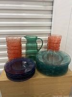 View of all items grouped on table showing the stacks of blue dinner and side plates, pink bowls, and the green pitcher.