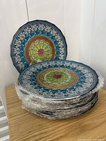 Stack of hand painted glass dinner plates showing intricate blue, green, and white ornate patterns with reddish center decoration.