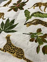 Close-up of pillow cover fabric showing embroidered leopard and tropical leaf design on white background.