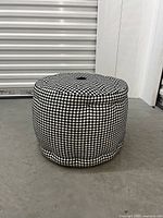 Perspective side view of one black and white houndstooth round floor cushion showing its tufted center and shape.
