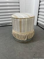 Full view of round ottoman showing fabric upholstery and fringe skirt