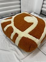 Close-up of tufted floor cushion showing brown base color and cream geometric pattern on the side and top.