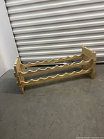 Front diagonal view of the wooden wine rack showing two shelves with carved wavy slots for wine bottles.