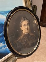 Oval framed portrait showing frontal view of an elderly woman with high collared Victorian dress, showing some damage on the surface and wear to the frame.