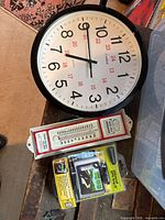 Photo of wall clock, refrigeration thermometer, and GPS car grip packaging on a wooden surface