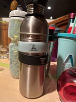 Close-up of two stainless steel water bottles with lids and carrying handles, one with a branding sticker.