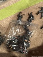 Miniature German soldier figures outside and inside plastic bags on a carpet surface displaying poses and detailed military uniforms