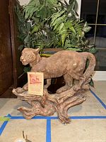 Side view of hand-carved cougar sculpture on twisted wood base with Dear Creek collection card showing.