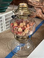Vintage-style floral glass lamp with dried petals inside and brass-colored metal top, resting on a carpet floor.