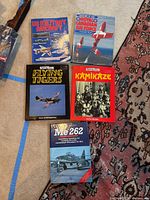 Five hardcover books displayed on carpet and floor: US Military Aircraft, Royal Canadian Air Force, Flying Tigers, Kamikaze, and Me 262.