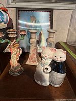 Overall view showing the cat couple milk jug, two artsy candle holders, angel candle holder, and framed holographic art piece in background.