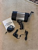 Rechargeable LED and halogen combo spotlight with charger, car charger adapter, and manual laid out on carpet.