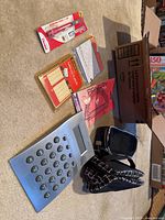 Photo showing large grey calculator, two pencil cases, assorted sticky notes, sticker book, eraser packaging, and other stationery items laid out on carpet.