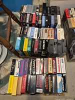 Three boxes of assorted VHS tapes visible with various movie titles including action and drama titles, box sets like Die Hard Double Feature Collection, and war documentaries.
