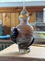 Front view of the vintage yellow and white swirled blown glass perfume bottle showing applied black glass arms wrapping the body and clear pointed stopper