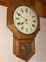 Vintage wooden wall clock with octagonal frame, Roman numeral dial, and brass pendulum visible through glass lower compartment