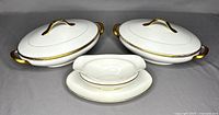 Photo showing set of two lidded oval bowls and a gravy boat with attached underplate. Gold trim on lid handles, bowl handles, rims, and gravy boat edges. White porcelain with some fading gold detail.