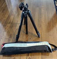 Manfrotto tripod set up standing on a wooden floor with carry bag beside it