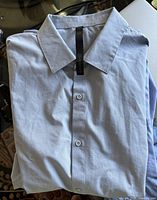 Folded light grey Lululemon men's long sleeve shirt laid on a surface showing collar, front button placket, and fabric texture.