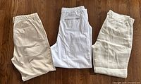 Four pairs of light-colored men's summer pants laid folded on wooden floor