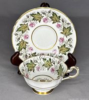 Front view of teacup in front of saucer showing floral leaf and rose pattern with gold trimming