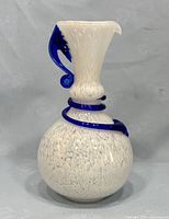 Front view of the vase showing white speckled spherical base with blue swirl and curved handle