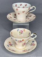 Two vintage Aynsley corset teacups with matching saucers, one set with tiny rose pattern and the other with multi-floral design.
