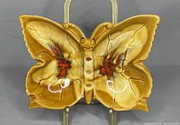 Front view of the butterfly shaped pottery ashtray showing detailed wings and painted red feather accents on a brown glazed surface.