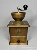 Front view of vintage Crosser coffee grinder showing the wooden base, brass grinding bowl, black knob on handle, and Crosser West German label on drawer.